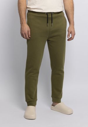 Olive green joggers with a drawstring waist, cuffed ankles, and side pockets. Made of soft, textured material. Paired with beige slip-on shoes.