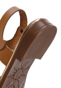Sandalo in pelle marrone con suola in gomma texturizzata, motivo circolare sulla soletta e un accento dorato lungo il tallone. Design aperto con cinturino alla caviglia.