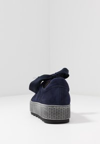 Zapatilla de ante azul marino con una suela de plataforma gruesa y texturizada, que presenta un lazo de tela en la parte trasera y una silueta redondeada.