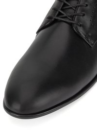 Czarne skórzane buty z wydłużonym noskiem, gładką fakturą i szczegółowym przeszyciem. Posiadają sznurowane zapięcie z perforowanymi akcentami.
