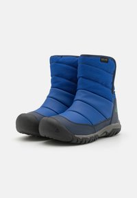 Blaue isolierte Stiefel mit nässefestem Nylon-Obermaterial, schwarzer Gummikappe und strukturiertem Sohlen. Mit grünem Logo an der Seite und Reißverschluss für einfaches An- und Ausziehen.