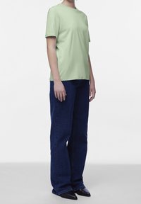 T-shirt di cotone verde chiaro con collo a giro e maniche corte, abbinata a jeans denim a gamba larga blu scuro e scarpe nere a punta.