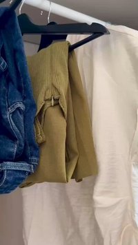 Hanging garments include a blue denim jacket, a green knitted sweater, and a light-colored blouse on a black hanger against a neutral background.