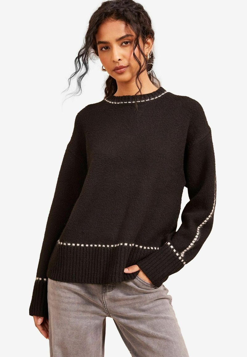 Maglione nero lavorato a maglia con scollo tondo, tessuto testurizzato e orlo a coste. Presenta cuciture bianche lungo le maniche e il bordo inferiore.