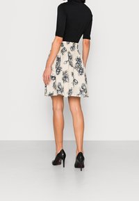 Top nero a maniche corte abbinato a una gonna floreale beige con motivi neri; la modella indossa scarpe con tacco nere.