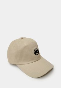 Gorra de béisbol beige hecha de tejido texturizado, con un logotipo circular negro en la parte frontal y un visor curvado. Presenta cinco orificios de ventilación.