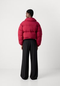 Μπορντό μπουφάν με ψηλό κολάρο, κοντά μανίκια και σχεδίαση με ραφές. Συνδυασμένο με φαρδιά μαύρα παντελόνια.