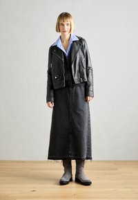 Svart skinn bikerjakke over et svart denim maxi skjørt. Lyseblå skjorte med krage under. Grå ankelstøvler med teksturert overflate.