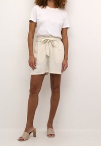 Linnen shorts in een lichte beige tint, met een strikdetail in de taille, zijzakken en een ontspannen pasvorm, gecombineerd met een wit t-shirt met ronde hals.
