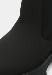 Svart vanntett ankelstøvel med en jevn, matt overflate og elastiske sidepaneler for enkel påkledning. Holdbar gummisåle gir godt grep.