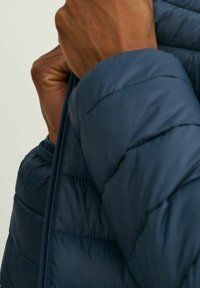 Doudoune bleu marine à matelassage horizontal, fermeture éclair et poignets élastiqués. Texture douce avec un design léger, idéal pour le superposition.