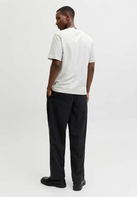 Hallide hallikas puuvillane t-särk, millel on lühikesed varrukad ja ümar kaelus, kantud koos mustade tõmblukuga pükstega. Siluett on lõdva istuvusega. Näha on mustad jalatsid.