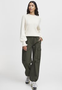 Pull en tricot texturé crème avec des manches bouffantes, associé à un pantalon cargo vert olive ample avec des poches latérales.