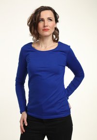 Camisa de manga larga azul en un estilo ajustado, hecha de una tela suave con un escote redondeado. Combinada con pantalones negros.