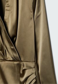 Satinowy materiał w oliwkowym kolorze z drapowaniami i marszczeniami, ukazujący część odzieży z długim rękawem.