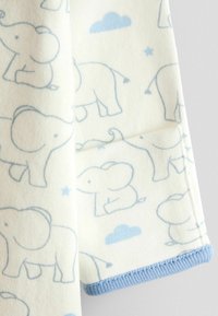 Blødt hvidt stof med lyseblå konturerede baby elefanter, små skyer, stjerner og blå kant langs kanten af et ærme på et tøjstykke.