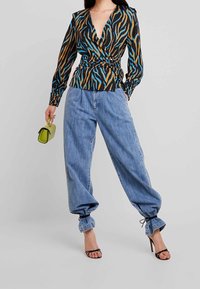 Blusa avvolgente con strisce zebrate nere, arancioni e blu, abbinata a pantaloni di denim baggy azzurri e sandali neri con tacco a strappo.