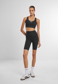 Schwarzer Sport-BH und passende High-Waist-Fahrradhosen, aus dehnbarem Stoff mit glatter Textur. Mit einem Logo auf der Vorderseite.