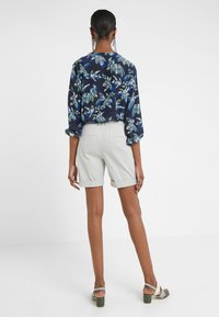 Marinblommig blus med gröna och blå mönster, tillsammans med ljusgrå uppvikta shorts. Modellen bär gröna klacksandaler.