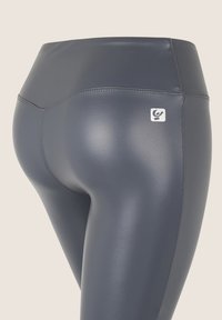 Leggings de talle alto en azul marino, hechos de un material suave y brillante. Presentan costuras cosidas y un pequeño logotipo de la marca en la cintura.