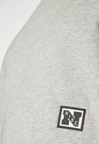 Sivi dukserica s teksturiranom tkaninom, na lijevoj strani ima ušiveni crno-bijeli Nike logo.
