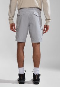 Pantalones cortos de cargo grises con bolsillos laterales, bolsillos traseros planos y un diseño hasta la rodilla. Combinados con zapatos negros y calcetines blancos.