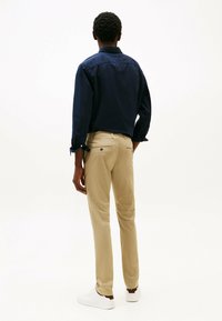 Navyblauwe langemouwen shirt met knoopmanchetten, gecombineerd met beige chino's en witte sneakers. De achterkant toont een gladde textuur.