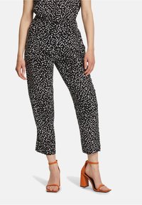 Czarne spodnie z białymi kropkami, z elastycznym pasem i skróconą długością. Połączone z pomarańczowymi sandałami na blokowym obcasie.