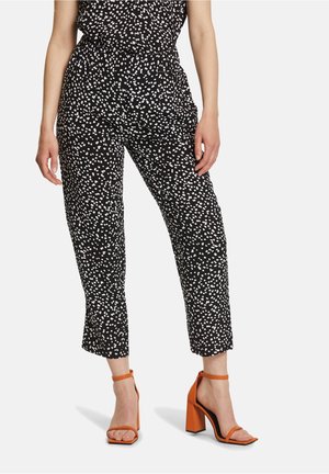 Pantalons noirs avec des éclaboussures blanches, dotés d'une taille élastique et d'une longueur raccourcie. Associés à des sandales à talons blocs orange.