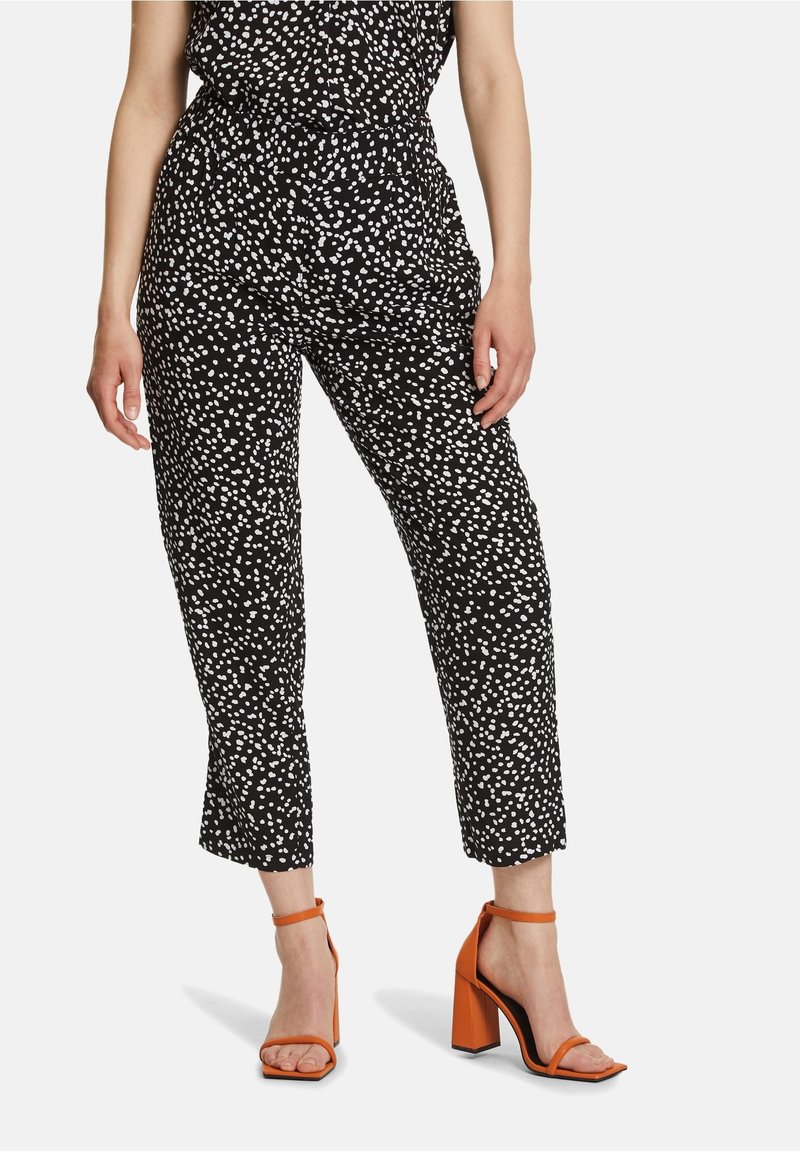 Czarne spodnie z białymi kropkami, z elastycznym pasem i skróconą długością. Połączone z pomarańczowymi sandałami na blokowym obcasie.