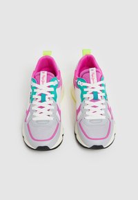 Sneaker colorati con parte superiore in rete grigia, dettagli in rosa e turchese, lacci bianchi e un tab sul tallone giallo brillante con suola nera.
