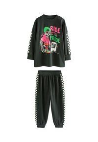 Haut noir à manches longues avec un design graphique représentant un squelette vêtu de vêtements colorés, accompagné d'un pantalon de jogging noir assorti avec des accents à carreaux.