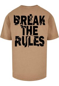 Beige bomulds T-shirt med stor sort grafisk tekst "BRYT REGLERNE" på ryggen, med skarpe, vinklede designs integreret i teksten.