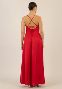 Rotes Satin-Kleid mit tiefem R�ückenausschnitt und überkreuzten Trägern. Das bodenlange Design hat einen fließenden Rock und eine gebundene Akzentuierung an der Taille.