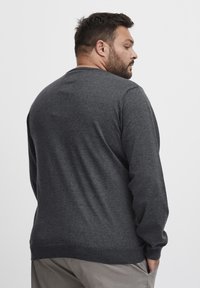 Pulover gri închis, fabricat dintr-un material tricotat texturat, cu mâneci lungi și decolteu rotund, având o margine și manșete ribbate.