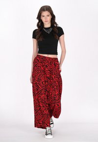 Rode en zwarte zebra-gestreepte wijde broek van lichtgewicht stof, gecombineerd met een aansluitend zwart crop top en zwart-witte sneakers.