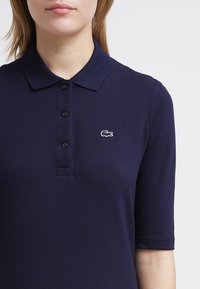 Mörkblå kortärmad polo med krage, i strukturväv, med tre knappar och en liten vit broderad logga på bröstet.