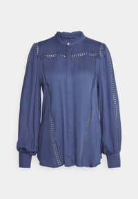 Blouse bleue à manches longues avec col haut volanté, fermeture par boutons et découpes décoratives en dentelle sur les manches et les panneaux avant.