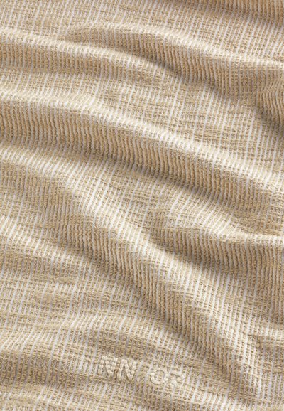 Tessuto testurizzato in beige con strisce chiare, caratterizzato da un motivo morbido e intrecciato. La superficie mostra profondità e una leggera texture in rilievo.