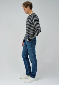 Camisa de manga larga a rayas blancas y negras, jeans azules y zapatillas blancas. La camisa tiene rayas horizontales y puños acanalados.
