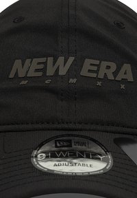 Fekete New Era sapka, amelynek elején domború betűk vannak. Tartalmaz egy kör alakú címkét, amelyen a "9TWENTY Állítható" felirat olvasható. Simára szőtt szövettextúra.