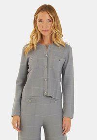 Giacca sweater grigia con texture, colletto rotondo, chiusura a bottoni e due tasche sul petto. Presenta bottoni decorativi. Motivo a quadri su tutta la stoffa.