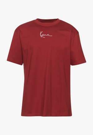 Sarkana kokvilnas T-krekls ar apaļu apkakli un īsām piedurknēm, kura priekšā ir balti izšūti burti. Mīksta tekstūra un brīvs piegriezums.