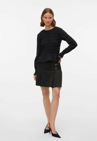 Sort langærmet top med smock og flæsekanter i kanten, kombineret med en mørk ternet mininederdel med dobbelte spænde-accenter og plisseret design.