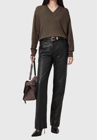 Sweter oliwkowy z dekoltem w serek, luźny fason, zestawiony z czarnymi, skórzanymi spodniami z wysokim stanem. Dodatek: brązowa torebka na ramię.