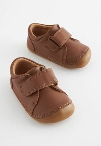 Chaussures en cuir marron pour tout-petits avec un bout rond, une sangle Velcro et une semelle en caoutchouc beige. Coutures détaillées le long des bords. Doublure douce visible.