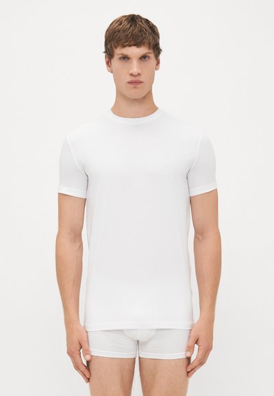 Weißes T-Shirt mit kurzen Ärmeln aus glattem Stoff; Rundhalsausschnitt, schlanker Schnitt und minimale Nähte mit dezentem Glanz. Kombiniert mit weißen Unterhosen.