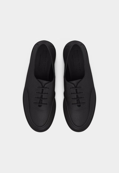 Ζευγάρι μαύρα δερμάτινα παπούτσια δετά με στρογγυλεμένες μύτες, σε θέα από πάνω σε ουδέτερο φόντο.