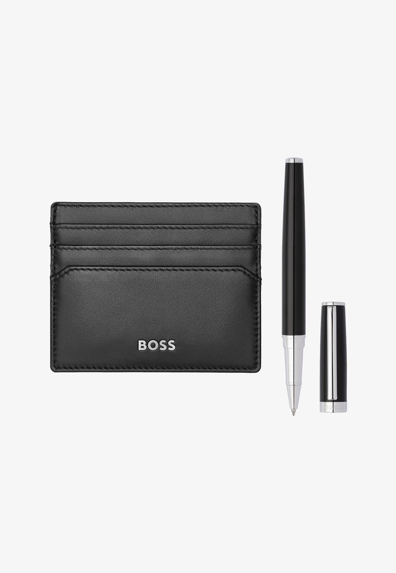 Porte-cartes BOSS en cuir noir avec quatre emplacements pour cartes à côté d'un stylo à bille noir et argent dont le capuchon est retiré.