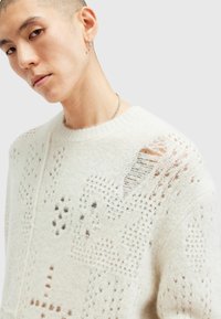Leichter weißer Pullover mit Strickstruktur, aufwendigen Mustern und einem kleinen abgenutzten Bereich an der Schulter. Runder Ausschnitt.